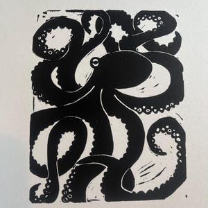 Peut inclure: Une linogravure en noir et blanc représentant un poulpe. Le poulpe a une tête arrondie et huit tentacules bouclés avec des ventouses. L'impression est sur fond blanc et de forme rectangulaire.