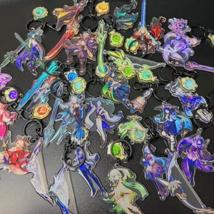 May include: A collection of acrylic keychains featuring various anime-style characters and weapons. The keychains have black metal rings and clasps. The designs include figures in shades of blue, purple, green, and red, with intricate details and transparent elements.