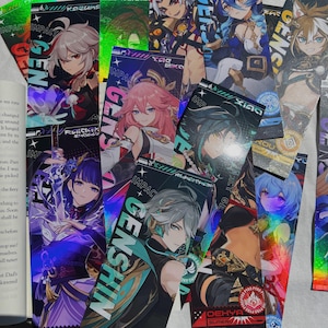 May include: A collection of colorful Genshin Impact character bookmarks. Each bookmark features a different anime-style character with vibrant colors and holographic accents. The word "GENSHIN" is prominently displayed on several bookmarks.