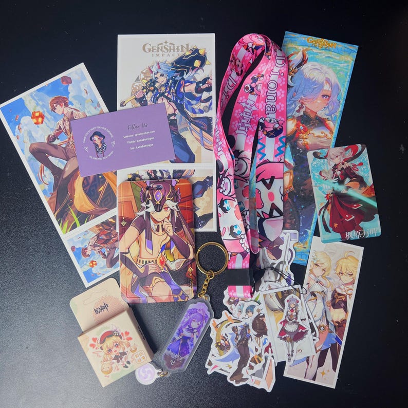 May include: A collection of Genshin Impact merchandise, including character art prints, a lanyard, stickers, a keychain, and a business card. The items feature vibrant colors and various character designs from the popular video game.