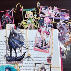Puede incluir: Una colección de marcadores de personajes de estilo anime. Cada marcador presenta un diseño de personaje único con colores vibrantes y detalles intrincados. Los marcadores están unidos a una cadena dorada y se colocan sobre un libro abierto.