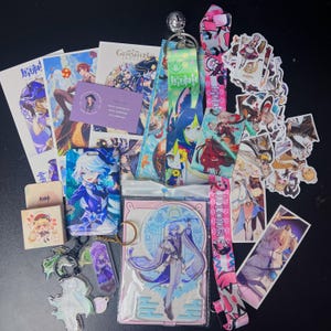 May include: A collection of Genshin Impact merchandise, including character art prints, stickers, keychains, and lanyards. The items feature various characters in vibrant colors, with a focus on anime-style illustrations. The items are arranged on a black surface.