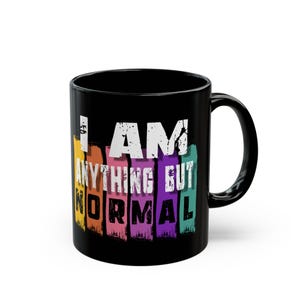 Puede incluir: Una taza de cerámica negra con un diseño gráfico vertical de cinco franjas de pinceladas de colores en amarillo, naranja, rosa, morado y turquesa. El texto blanco dice I AM ANYTHING BUT NORMAL, con la palabra NORMAL en letras negras negritas.