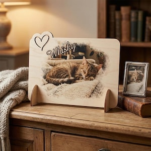Può includere: Cornice in legno con un ritaglio a forma di cuore e il nome "Whisky" in corsivo. La cornice mostra una foto a colori di un gatto tabby che dorme. Una foto più piccola incorniciata del gatto è su una superficie di legno.