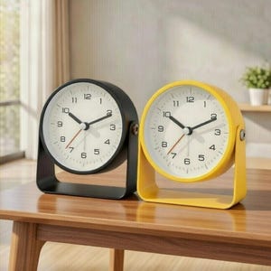 May include: Two small, round alarm clocks, one black and one yellow, each with a white face and black numerals. The clocks are approximately 3 inches in diameter and sit on a wooden surface. The text "3 inch creative rotation - small alarm clock" is above the clocks.