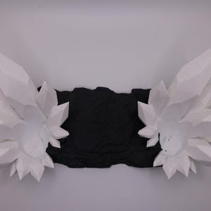 May include: A pair of white, geometric crystal sculptures with sharp, angular facets. The crystals are arranged on either side of a textured black base, creating a symmetrical design. The background is a plain white surface.