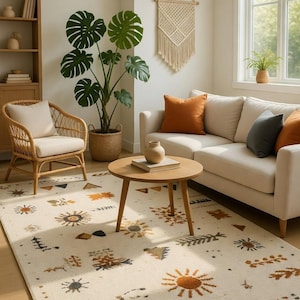 May include: A living room scene featuring a cream-colored rug with a sunburst pattern, a light-colored sofa with orange and gray pillows, and a round wooden coffee table. A wicker chair and a large potted plant add to the room's decor.