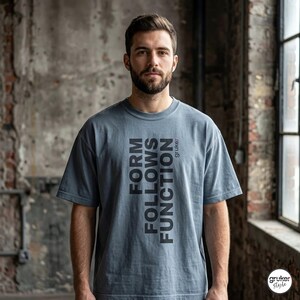 Può includere: Una t-shirt a maniche corte color blu ardesia con il testo verticale nero "FORM FOLLOWS FUNCTION" stampato sul davanti, con il piccolo logo rosso e nero "gruke:" posizionato vicino alla parte superiore destra del blocco di testo.