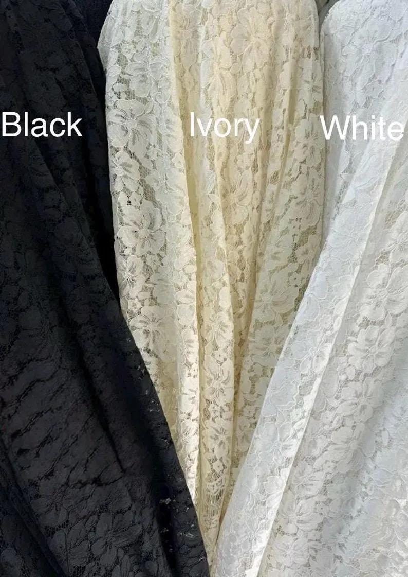 May include: Three vertical panels of floral lace fabric displayed side by side. The left panel is black, the center panel is ivory, and the right panel is white. The text Black, Ivory, and White is printed over each respective fabric color.