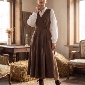 Peut inclure: Une robe portefeuille sans manches marron avec un décolleté en V, une taille ceinturée et une jupe plissée, portée sur une chemise blanche à manches longues et col, associée à des bottines à lacets marron à talons.