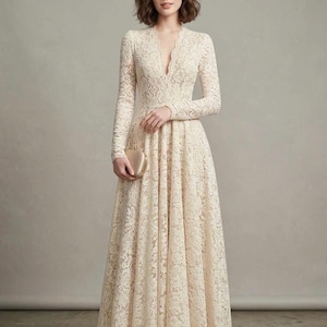 May include: A floor-length cream-colored lace dress featuring long sleeves, a deep V-neckline, and a fitted bodice that transitions into a full, flowing skirt. The garment is paired with a small, smooth, metallic gold-toned clutch and pointed-toe heels.