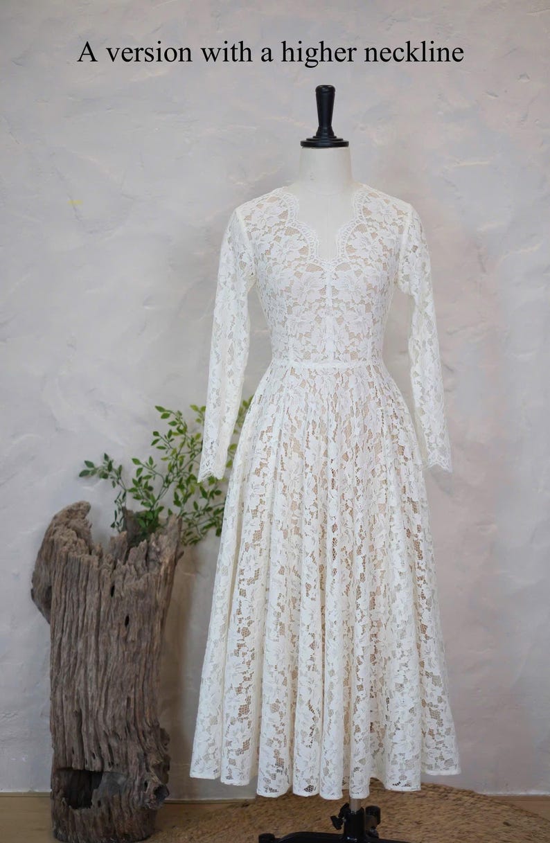 May include: A white lace dress with long sleeves, a V-neckline, and a fitted bodice that transitions into a full, pleated skirt. The dress is displayed on a mannequin and features the text A version with a higher neckline at the top.