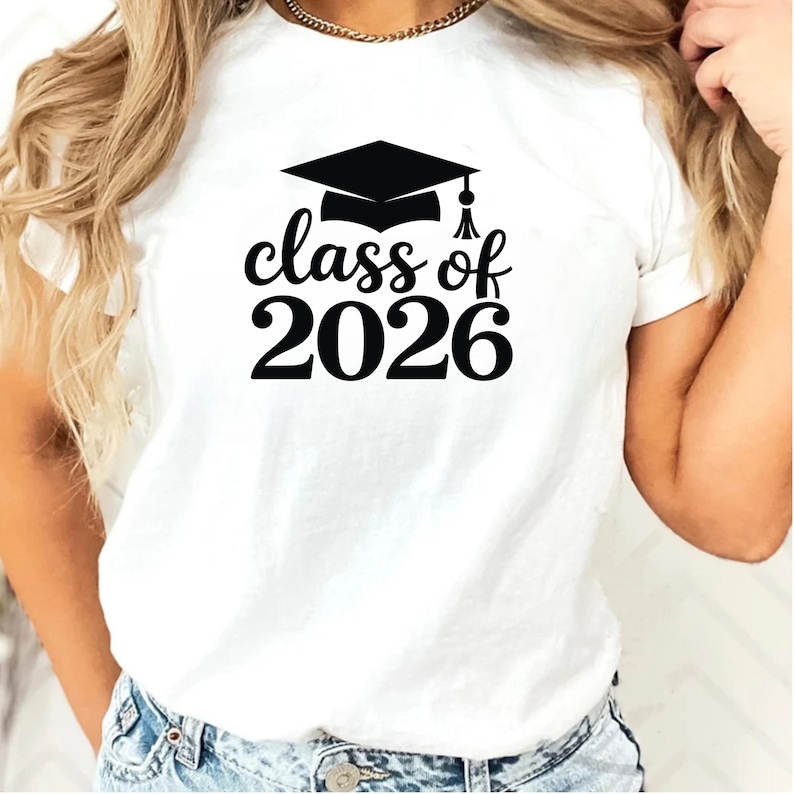 May include: White t-shirt featuring a black graduation cap and the words "class of 2026". The design is centered on the front of the shirt. The shirt is made of a soft material.