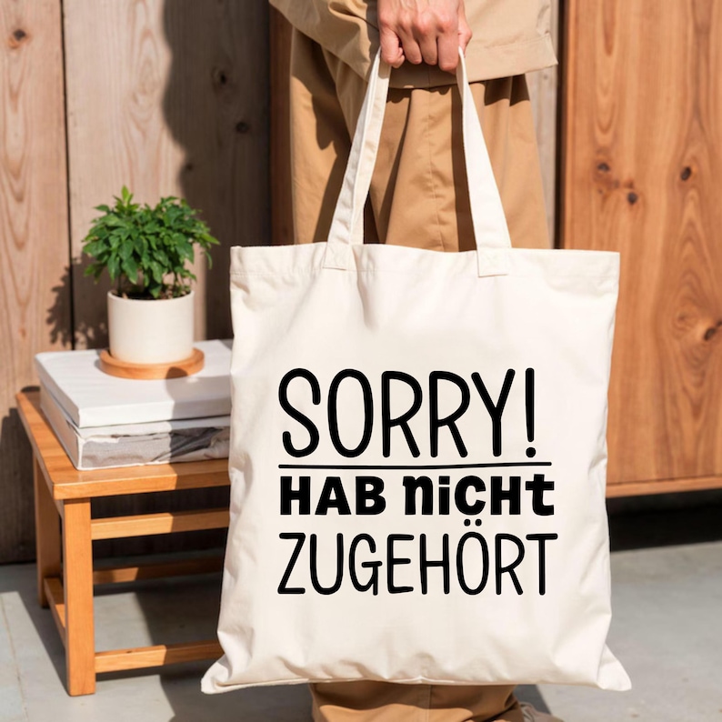 May include: A cream-coloured canvas tote bag featuring the black printed text SORRY! HAB nicht ZUGEH&Ouml;RT. The bag has two long shoulder straps and a rectangular shape, constructed from a woven fabric material with a clean, simple design.