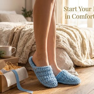 May include: Light blue crochet slippers are worn indoors. The image also shows a bed with a beige knitted blanket, a mug, and a gift box with a blue ribbon. The text "Start Your Day in Comfort" is displayed.