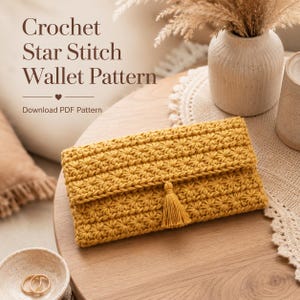 Puede incluir: Cartera de ganchillo de color amarillo mostaza con un patrón de punto de estrella y una borla. La cartera está sobre una mesa de madera con el texto "Crochet Star Stitch Wallet Pattern" y "Download PDF Pattern".