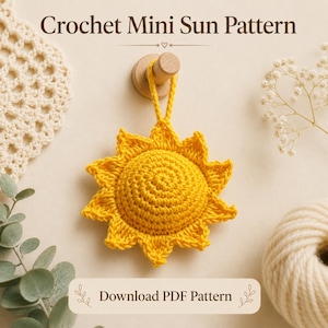 Pode incluir: Um sol amarelo brilhante de crochê, com um centro em espiral e raios pontiagudos, pendurado em um pino de madeira. O texto diz "Crochet Mini Sun Pattern" e "Download PDF Pattern". Uma decoração alegre e artesanal.