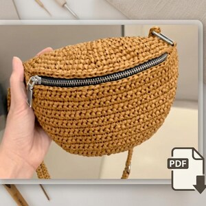 May include: A woven, tan-colored fanny pack with a black zipper and silver zipper pull. The bag is held by a hand and has a strap. The bag is made of a woven material and has a rounded shape. The bag is a PDF download.