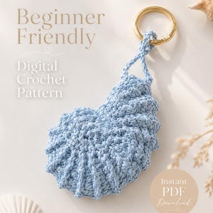 May include: A light blue, crocheted seashell-shaped keychain with a gold-colored ring. The image includes text that reads "Beginner Friendly" and "Digital Crochet Pattern". A small, round sticker says "Instant PDF Download".