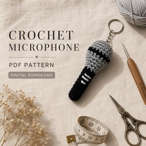 May include: A crochet microphone keychain featuring a grey mesh head and a black handle with white accents. The text CROCHET MICROPHONE PDF PATTERN DIGITAL DOWNLOAD is visible. A wooden crochet hook, scissors, and a measuring tape are present.