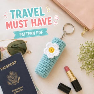 Puede incluir: Un llavero portalabiales de ganchillo azul claro con una flor blanca de centro amarillo. El texto TRAVEL MUST HAVE PATTERN PDF aparece sobre el objeto, rodeado de gafas de sol, un pasaporte y un pintalabios.