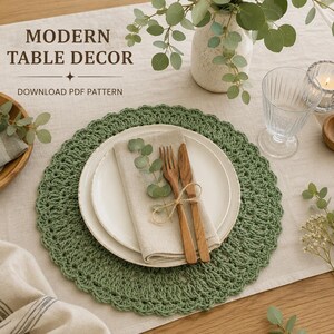 May include: A round sage green crocheted placemat featuring a scalloped edge, topped with a white ceramic plate, a beige linen napkin, and wooden cutlery. The text MODERN TABLE DECOR DOWNLOAD PDF PATTERN is visible in the upper left corner.