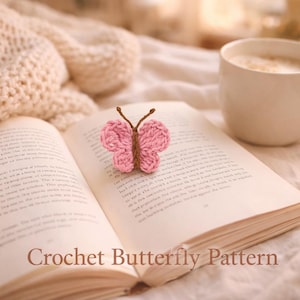May include: A pink and brown crochet butterfly rests on an open book. The book is on a cream-colored surface, with a white mug of coffee nearby. The text "Crochet Butterfly Pattern" is visible at the bottom of the image. The scene has a warm, cozy aesthetic.