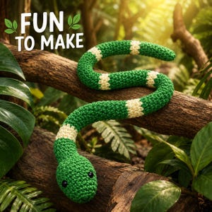 Puede incluir: Un juguete de serpiente tejido a ganchillo en color verde y crema con ojos de cuentas negras, que presenta un patrón de rayas repetitivo a lo largo del cuerpo. El texto "FUN TO MAKE" aparece en letras blancas con iconos de hojas verdes.