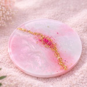 Peut inclure: Un dessous de verre rond décoratif avec un motif marbré rose et blanc. Un accent doré pailleté et rose traverse le centre. Le dessous de verre mesure environ 10 cm de diamètre.