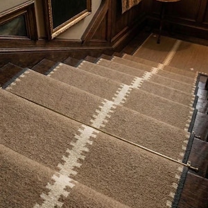 May include: A tan stair runner with a central white zigzag pattern and dark grey edges, secured to wooden stairs with metallic rods. The runner features a textured weave and covers the centre of each step, extending down the staircase.