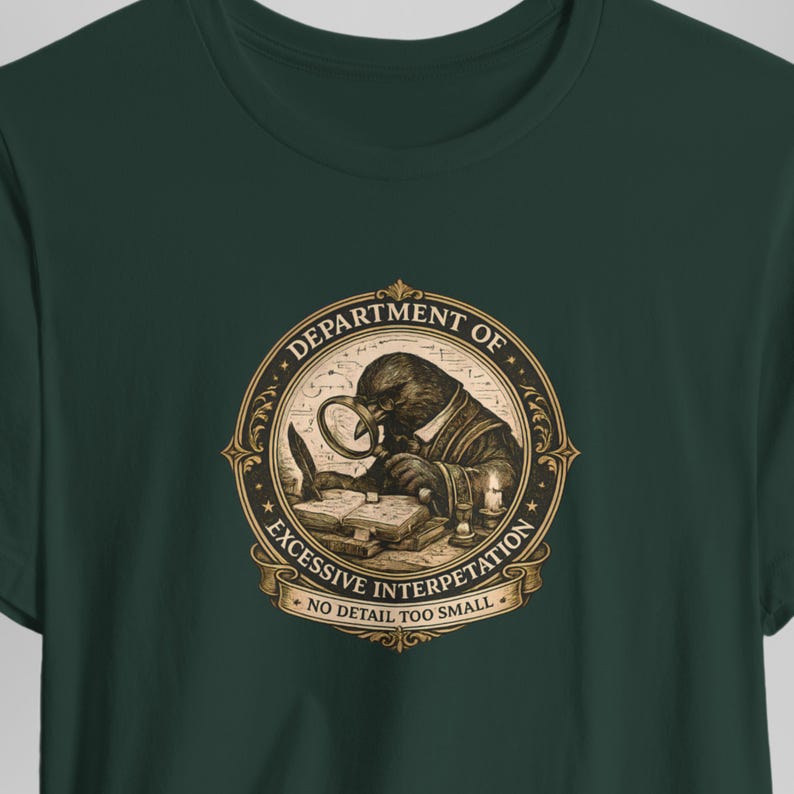 May include: A dark green t-shirt featuring a circular gold and black graphic of a crow looking through a magnifying glass at an open book. The text reads DEPARTMENT OF EXCESSIVE INTERPRETATION and NO DETAIL TOO SMALL in a decorative frame.