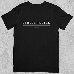 May include: Black t-shirt with the white text "STRESS TESTED" above a white line. The brand name "DryLogic" is printed in white below the line. The shirt is displayed on a light gray background.