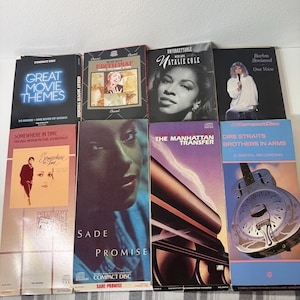 May include: A collection of eight rectangular music compact disc longbox cases featuring various album covers including Great Movie Themes, Edith Piaf, Natalie Cole, Barbra Streisand, Somewhere in Time, Sade Promise, The Manhattan Transfer, and Dire Straits.