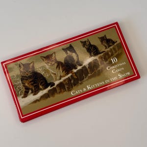 May include: A rectangular box of 10 Christmas cards featuring a gold-toned illustration of four tabby kittens sitting on a stone wall covered in snow. The box has a red border and the text "10 Christmas Cards Cats & Kittens in the Snow".