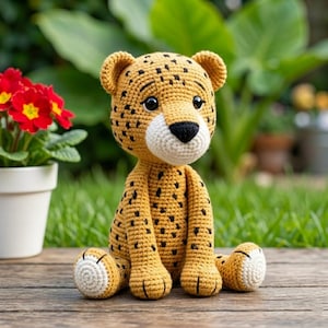 May include: A handmade crochet cheetah toy in a sitting position. The cheetah is primarily yellow with black spots, a white muzzle, and a black nose. The toy has a friendly expression and is sitting on a wooden surface.