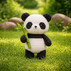 May include: A handmade crochet panda bear with black and white coloring, holding a green bamboo stalk with leaves. The panda has black eyes and ears. The plush toy is standing on green grass.