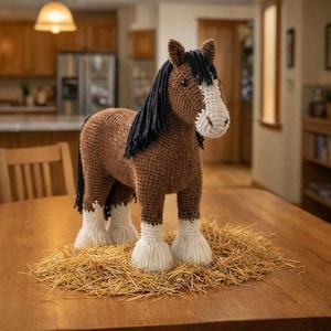 Könnte beinhalten: Eine handgefertigte Häkelpferdefigur. Das Pferd ist braun mit schwarzer Mähne und Schweif sowie weißen Abzeichen an Gesicht und Beinen. Es steht auf einem Strohbett und schafft eine rustikale und charmante Präsentation. Das Pferd ist etwa 30 cm hoch.
