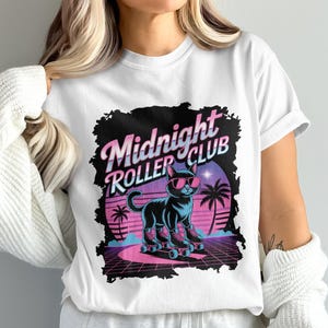 May include: White t-shirt featuring a retro graphic of a black cat wearing sunglasses and roller skates. The design includes the text "Midnight Roller Club" in a stylized font, with a neon color scheme and palm trees.