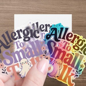 Hand holding clear stickers with "Allergic To Small Talk" text and cartoon ghosts.