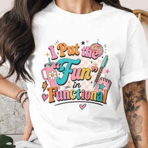 以下が含まれることがあります： 「I Put the Fun in Functional」と書かれたカラフルなグラフィックが特徴の白いTシャツ。デザインには、デイジーのピンクのマグカップ、ディスコボール、ペン、メモ帳が含まれています。テキストはさまざまな色とフォントです。