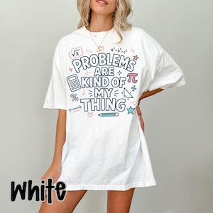 Könnte beinhalten: Ein weißes kurzärmeliges T-Shirt mit einem Grafikdruck, der den Text "PROBLEMS ARE KIND OF MY THING" in Dunkelblau zeigt. Das Design enthält verschiedene mathematische Symbole wie einen Taschenrechner, einen Stift und Pi.
