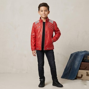 May include: A bright red jacket featuring a stand-up collar, multiple silver-toned zippered pockets on the chest and sleeves, and textured shoulder panels. The jacket is worn over a black shirt with dark denim jeans and black sneakers.