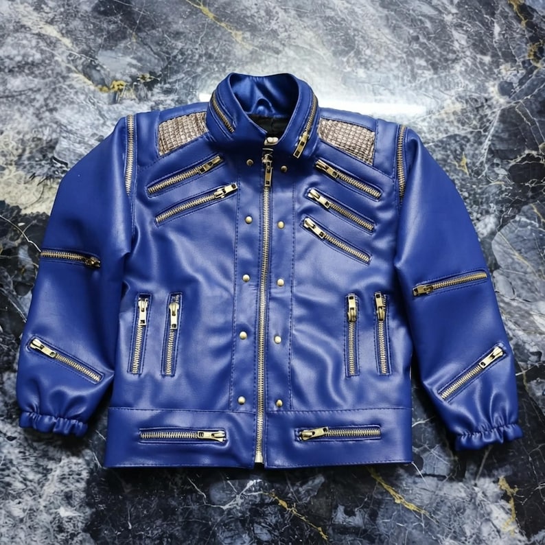 May include: A blue jacket featuring a high collar, long sleeves with elastic cuffs, and a front zipper closure. The garment is adorned with multiple gold-toned zippers across the chest and sleeves, along with metallic studs and textured panels.