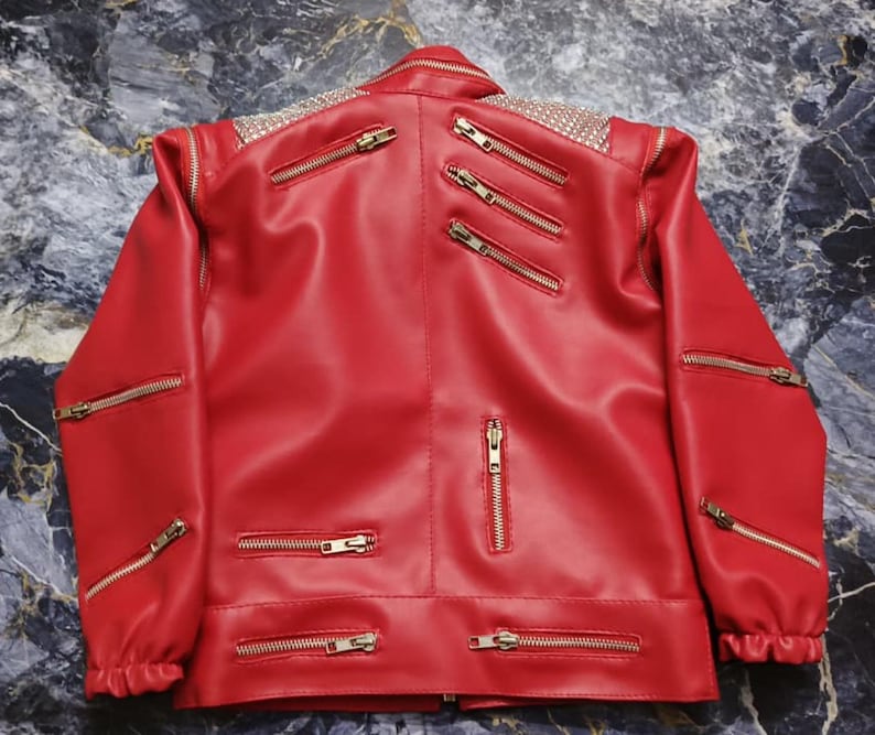 May include: A bright red jacket featuring multiple gold-toned metal zippers across the front, sleeves, and chest. The shoulders are embellished with a dense pattern of small, reflective silver studs, and the cuffs are gathered with elastic.