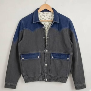 Puede incluir: Una chaqueta vaquera de dos tonos con canesú y solapas de bolsillo en azul oscuro que contrastan con un cuerpo gris carbón. La chaqueta incluye cierre frontal de botones, cuello en punta y forro interior con estampado de pequeños óvalos.