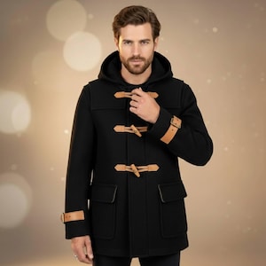 May include: Black duffel coat with a hood and toggle closures. The coat features two front pockets and leather accents on the toggles and cuffs. The coat is a classic outerwear piece.