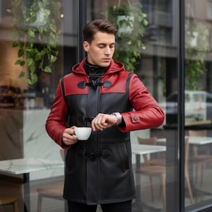 May include: A black and red leather hooded coat with toggle fastenings. The coat features red sleeves and a black body. The person in the image is holding a white coffee cup and checking their watch. The coat is a stylish outerwear garment.