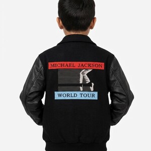 May include: A black varsity jacket with black leather sleeves and a ribbed collar. The back features a rectangular red patch with the text MICHAEL JACKSON, a graphic of a white piano keyboard, and a light blue patch with the text WORLD TOUR.