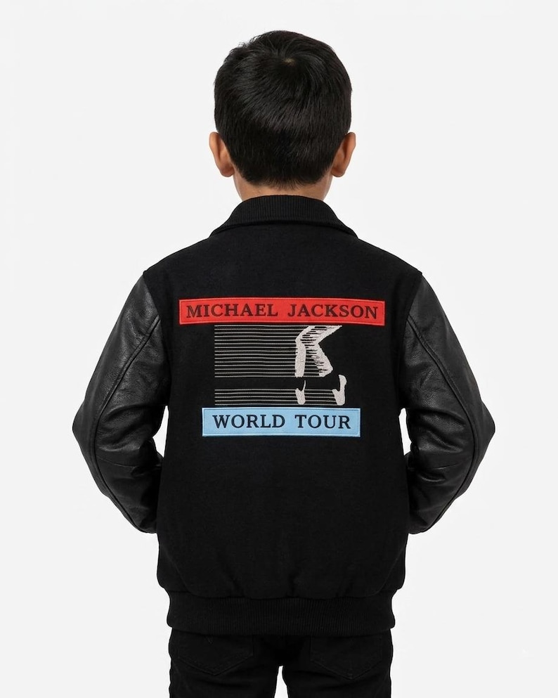 May include: A black varsity jacket with black leather sleeves and a ribbed collar. The back features a rectangular red patch with the text MICHAEL JACKSON, a graphic of a white piano keyboard, and a light blue patch with the text WORLD TOUR.