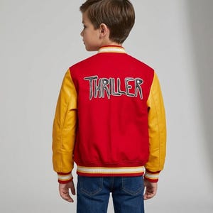 May include: A red varsity jacket with yellow sleeves and striped ribbed trim at the collar, cuffs, and hem. The back features the word THRILLER in large, stylized white and black lettering. The jacket is worn over blue denim jeans.